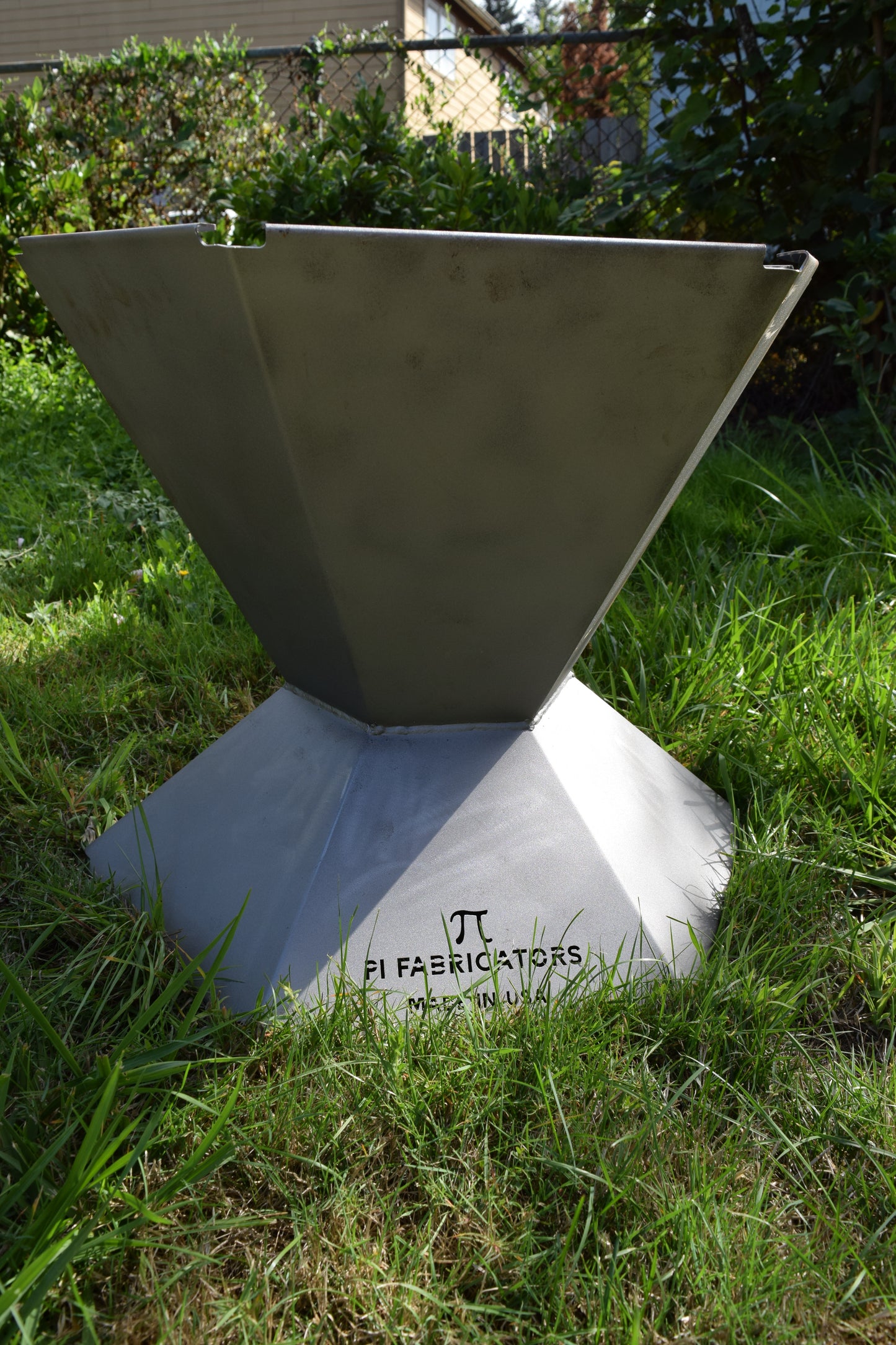 Biochar fire pit pictured from side in grass lawn. Sun shining from right side of image.