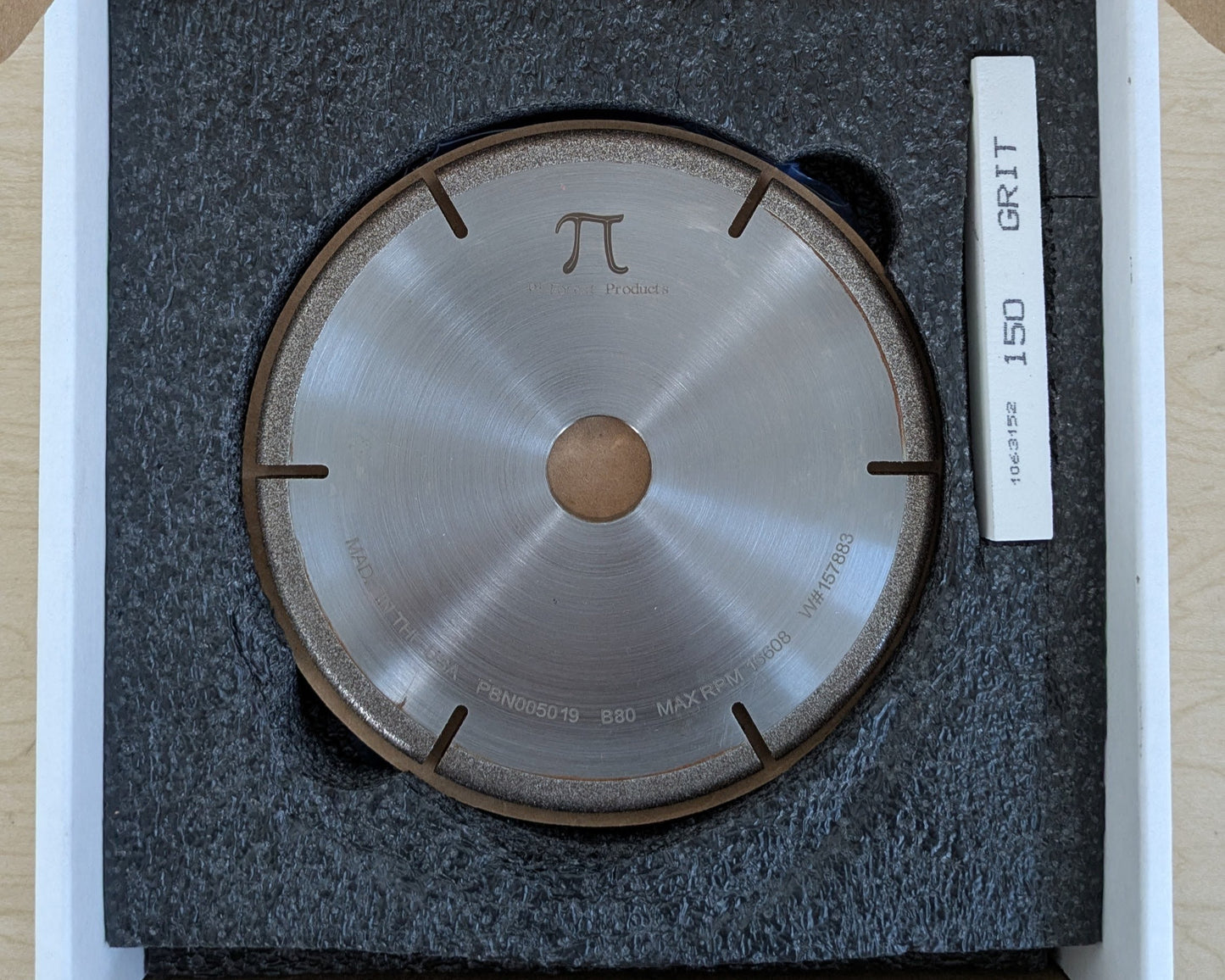 A CBN grinding wheel and a white dressing stick packaged together inside a cardboard shipping box