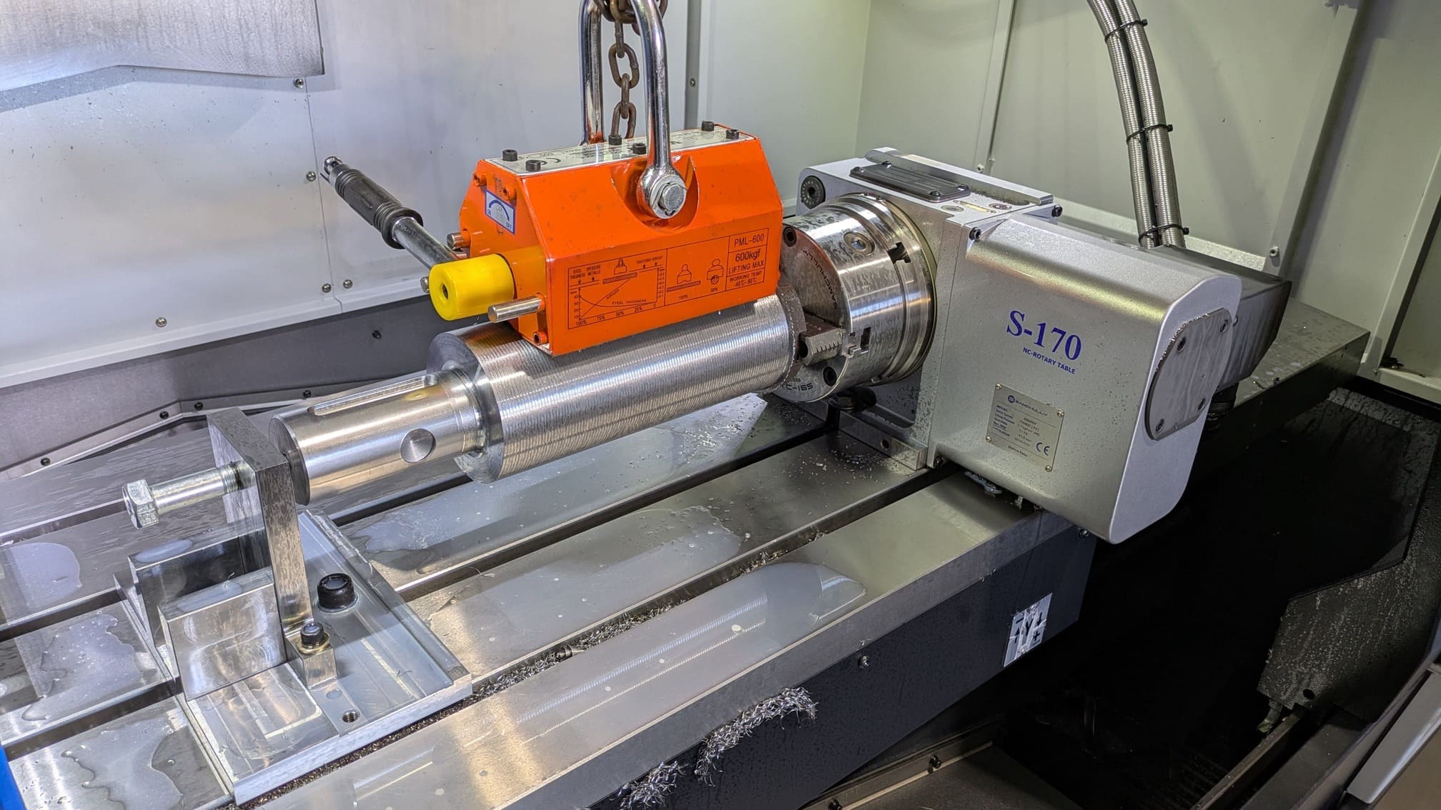 Machined tip of an auger shaft, held by a lifting magnet in preparation for removal from the CNC machine's 4th axis.