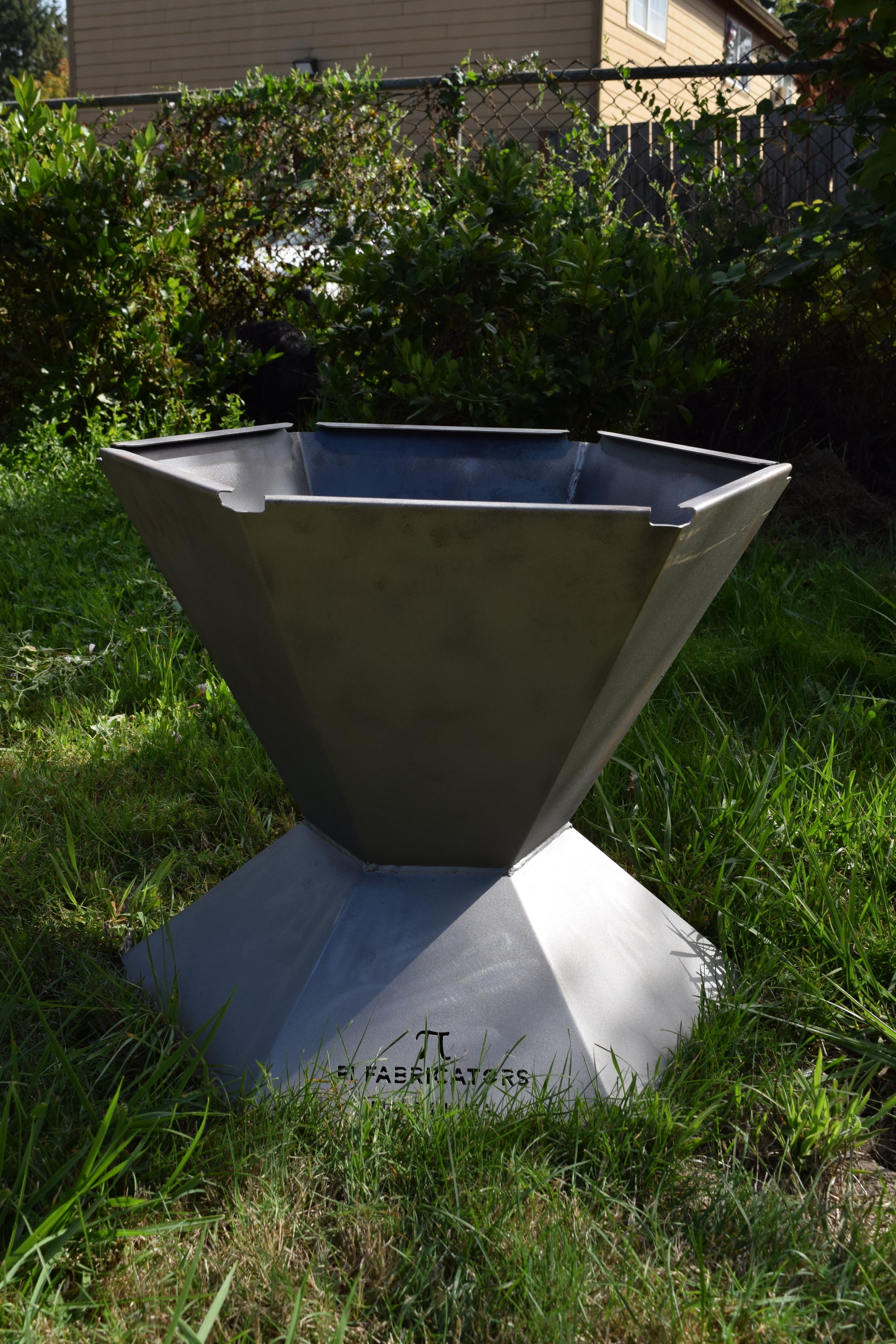 Front view of the Biochar Fire Pit  with grass and a fence in the background. 