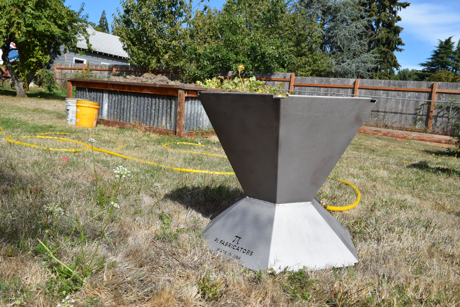 Biochar fire pit sitting on grass. Pi Fabricators branding visible.