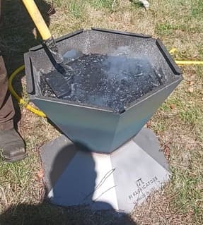 Pi Fabricators biochar kiln, Made in USA, shown filled with water and biochar after quenching. A hoe is being used to mix and submerge the floating hot coals into the water.