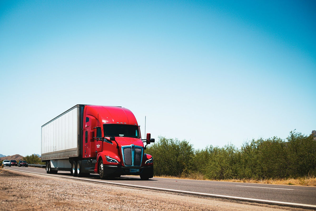 A red semi truck with a dry van trailer on a country road