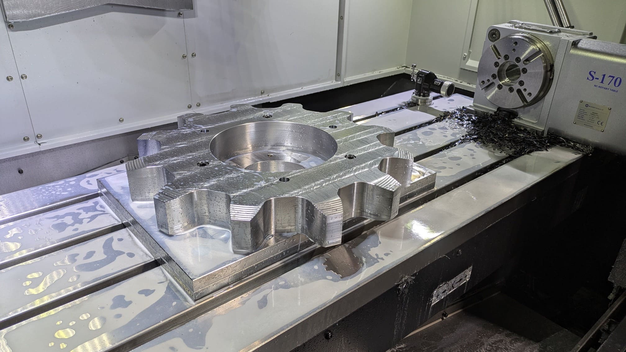 Large sprocket for wood products conveyor chain, with the 4th axis of a CNC machine visible in the background.